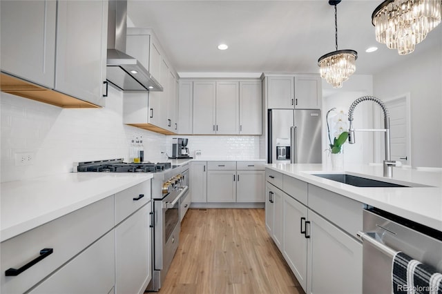 kitchen featuring wall chimney range hood, high quality appliances, light countertops, a chandelier, and a sink