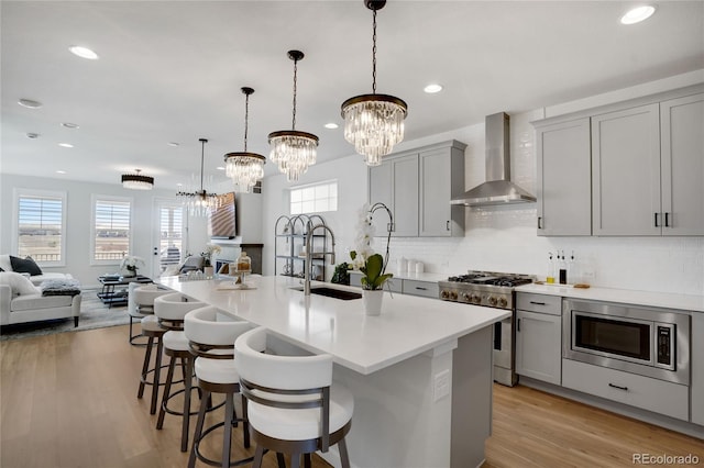 kitchen with open floor plan, wall chimney range hood, a notable chandelier, gray cabinetry, and stainless steel appliances