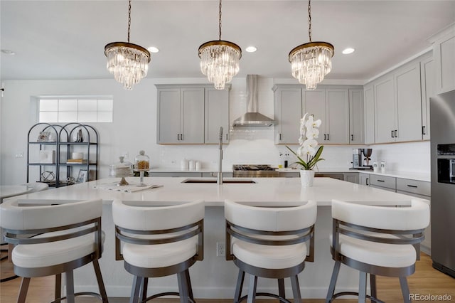 kitchen with a sink, stainless steel fridge with ice dispenser, light countertops, a chandelier, and wall chimney exhaust hood