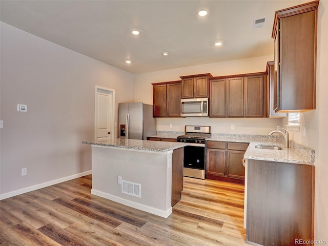 kitchen featuring visible vents, a center island, appliances with stainless steel finishes, light wood-style floors, and a sink