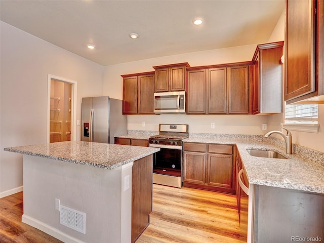 kitchen featuring light wood finished floors, appliances with stainless steel finishes, a center island, and a sink