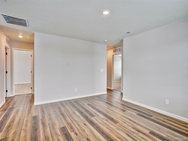 empty room with wood finished floors, visible vents, and baseboards