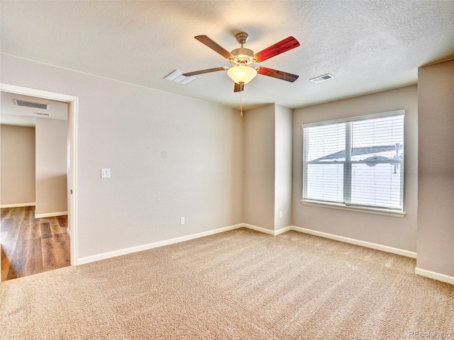 carpeted spare room featuring visible vents, baseboards, a textured ceiling, and a ceiling fan