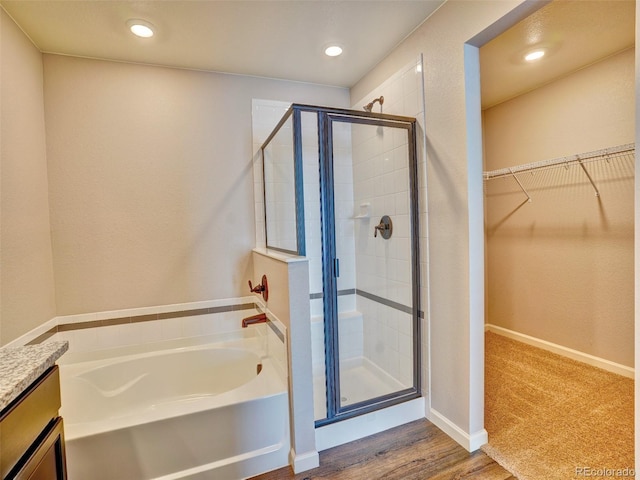 bathroom featuring a spacious closet, a shower stall, vanity, and a garden tub