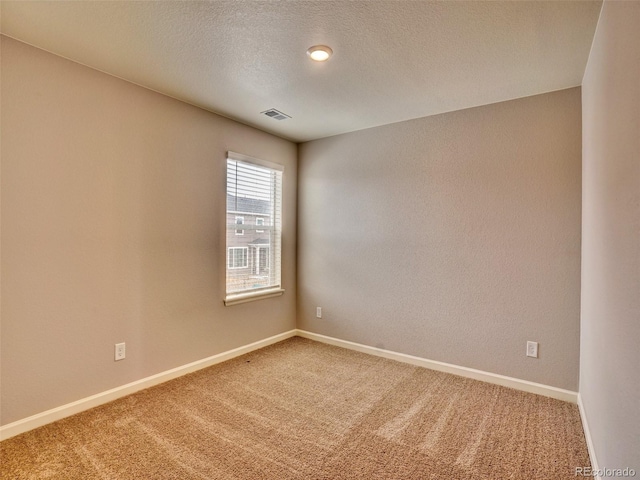 unfurnished room featuring visible vents, light colored carpet, a textured ceiling, and baseboards