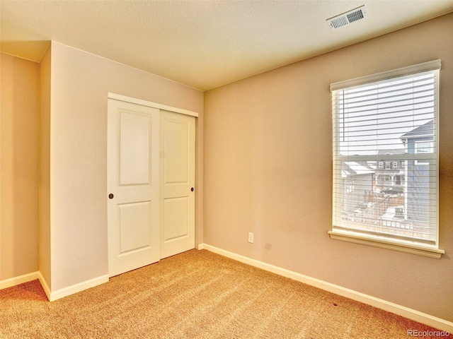 unfurnished bedroom featuring a closet, visible vents, light colored carpet, and baseboards