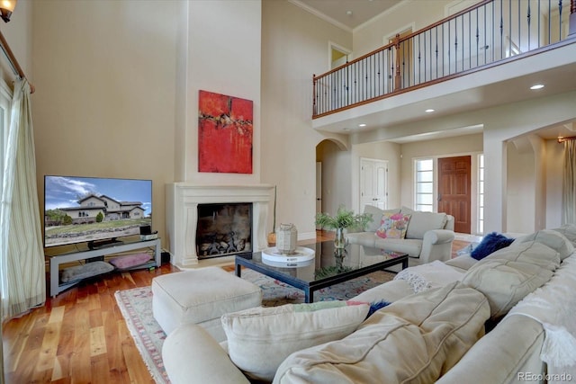 14993 W 55th Dr, Golden, CO 80403 - living room with arched walkways, a towering ceiling, wood finished floors, a fireplace with raised hearth, and ornamental molding