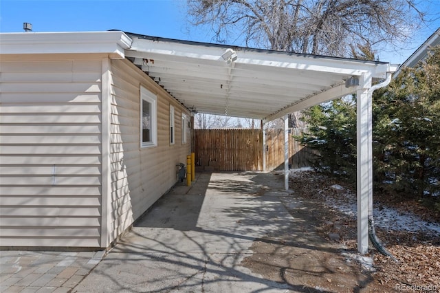 view of patio featuring driveway, an attached carport, and fence