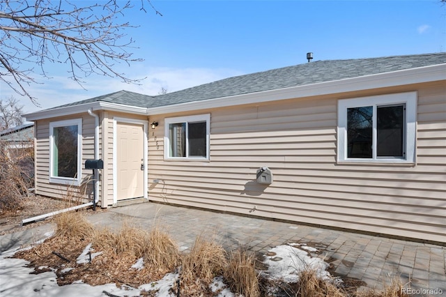 snow covered property featuring a patio area and roof with shingles