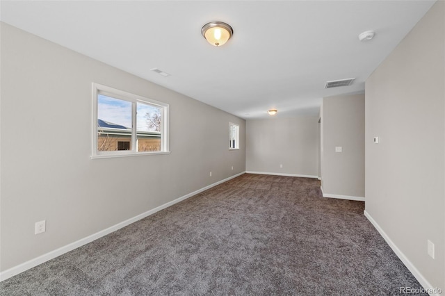 empty room featuring dark colored carpet, visible vents, and baseboards