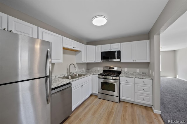 kitchen featuring light stone countertops, white cabinetry, stainless steel appliances, and a sink