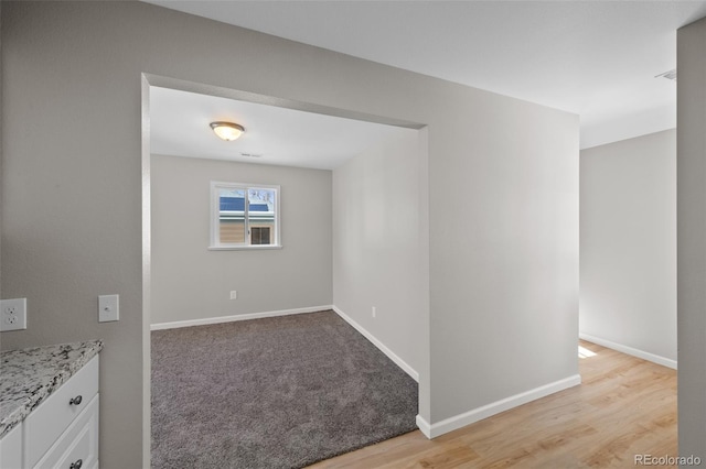 spare room featuring light wood-style floors, baseboards, and light colored carpet