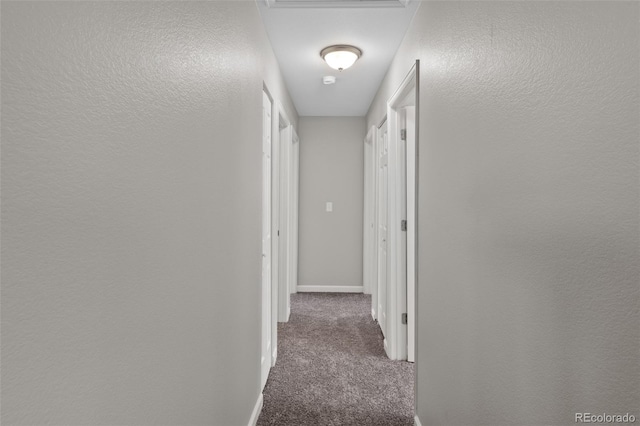 hall with dark colored carpet, a textured wall, and baseboards