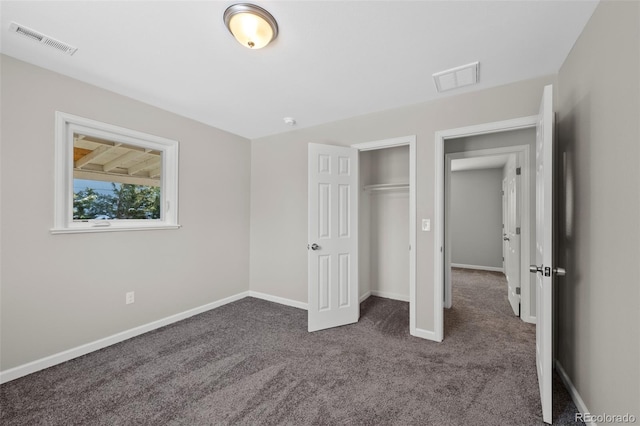 unfurnished bedroom with baseboards, visible vents, dark colored carpet, and a closet