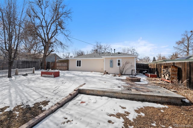 snow covered rear of property featuring a fenced backyard and a fire pit