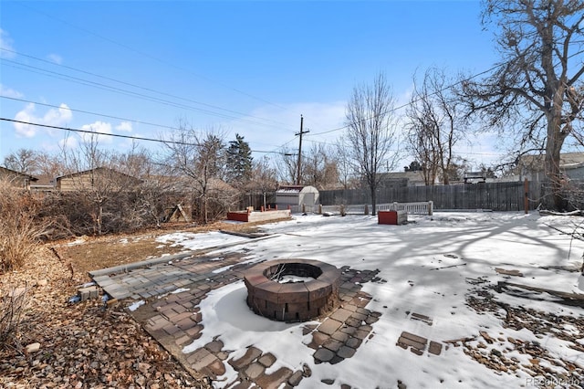 yard layered in snow with a storage unit, fence, a fire pit, and an outbuilding