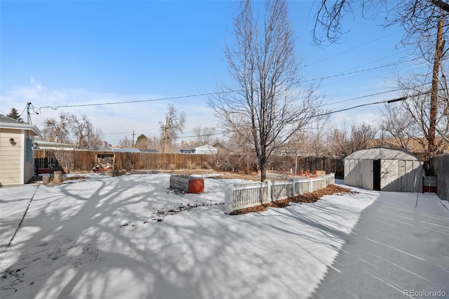 yard layered in snow featuring an outbuilding, a fenced backyard, and a shed