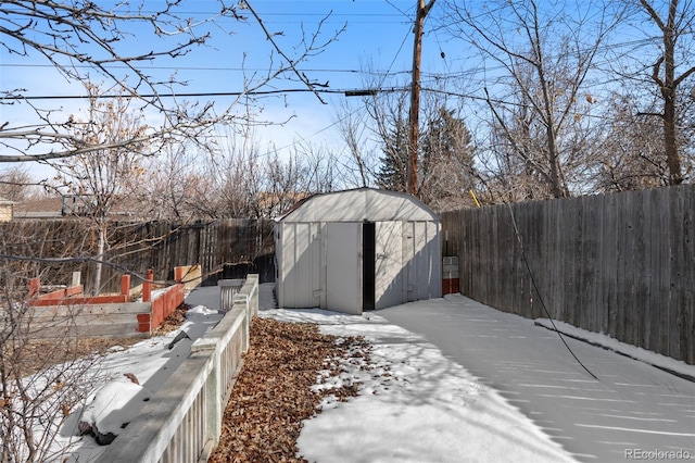 snowy yard with an outbuilding, a fenced backyard, and a storage unit