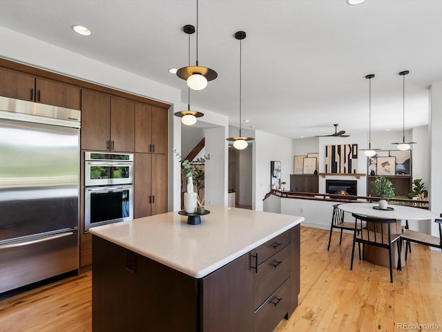 10057 S Shadow Hill Dr, Lone Tree, CO 80124 - kitchen with stainless steel appliances, a glass covered fireplace, hanging light fixtures, light wood-style flooring, and recessed lighting