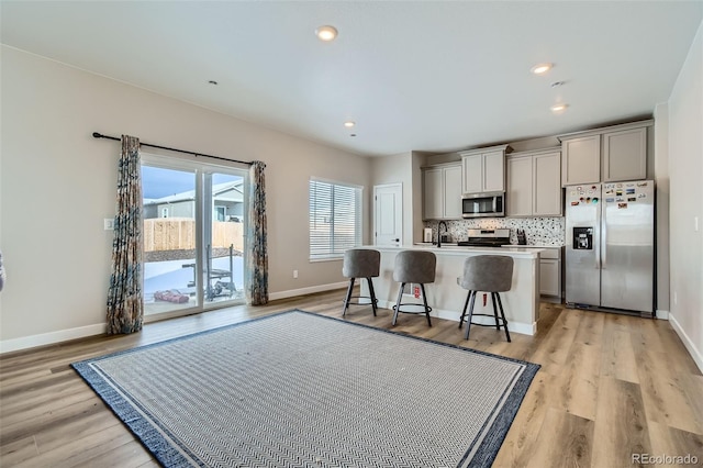 kitchen with stainless steel appliances, gray cabinets, light hardwood / wood-style floors, a breakfast bar, and a kitchen island with sink