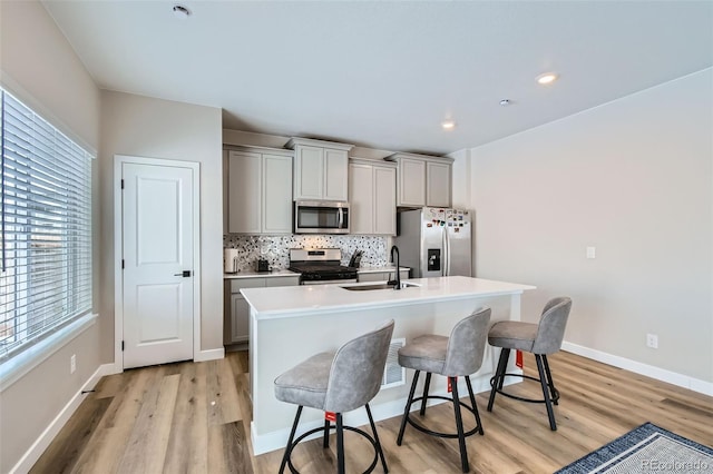 kitchen with an island with sink, stainless steel appliances, sink, and gray cabinetry