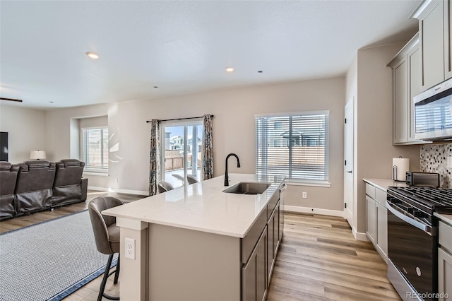 kitchen with stainless steel appliances, light hardwood / wood-style floors, sink, a kitchen bar, and a kitchen island with sink