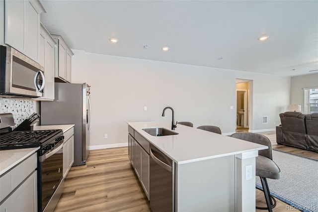 kitchen featuring a center island with sink, sink, a kitchen breakfast bar, light wood-type flooring, and appliances with stainless steel finishes