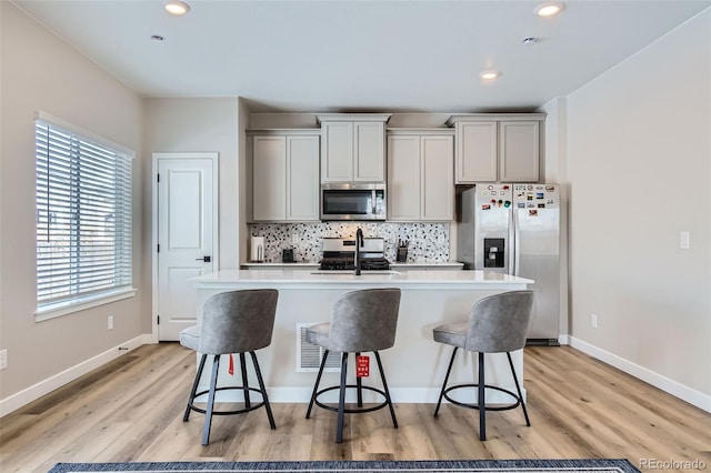 kitchen featuring a kitchen bar, gray cabinets, appliances with stainless steel finishes, and light hardwood / wood-style floors