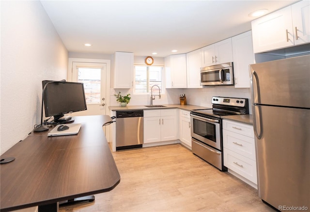 kitchen with appliances with stainless steel finishes, a sink, white cabinets, tasteful backsplash, and light wood-type flooring