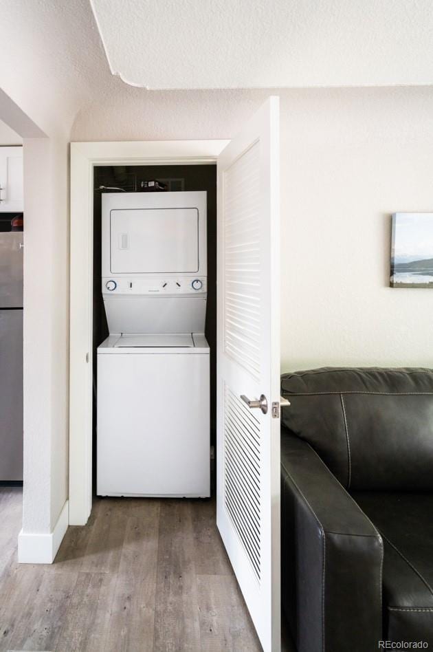laundry area featuring stacked washer / drying machine, wood finished floors, and baseboards