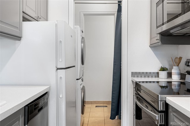 kitchen featuring gray cabinetry, light tile patterned floors, stainless steel appliances, and stacked washer and clothes dryer