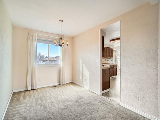 empty room with a textured ceiling, a notable chandelier, and light carpet