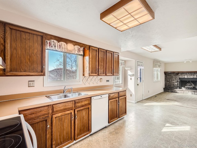 kitchen with stove, a textured ceiling, white dishwasher, sink, and a stone fireplace