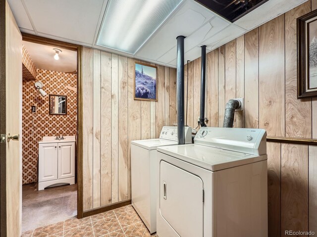 clothes washing area featuring light tile patterned flooring, separate washer and dryer, and wooden walls