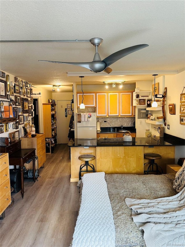 kitchen featuring dark countertops, wood finished floors, a peninsula, a textured ceiling, and white fridge