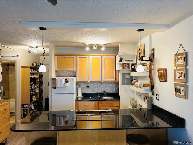 kitchen with a textured ceiling, a sink, freestanding refrigerator, tasteful backsplash, and decorative light fixtures