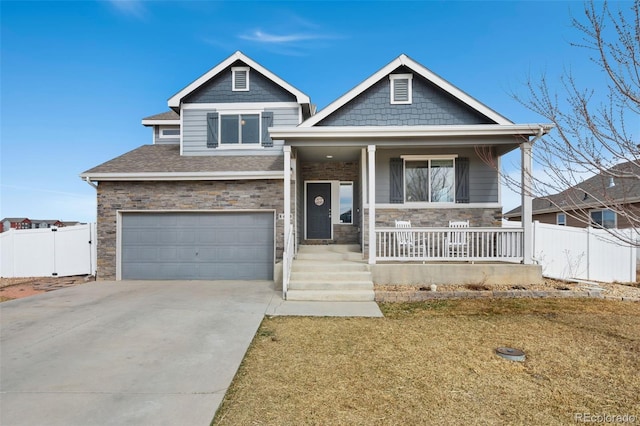 view of front facade with covered porch, stone siding, concrete driveway, an attached garage, and fence
