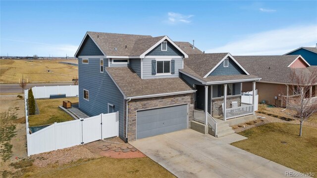 view of front of house featuring a gate, covered porch, stone siding, concrete driveway, and fence