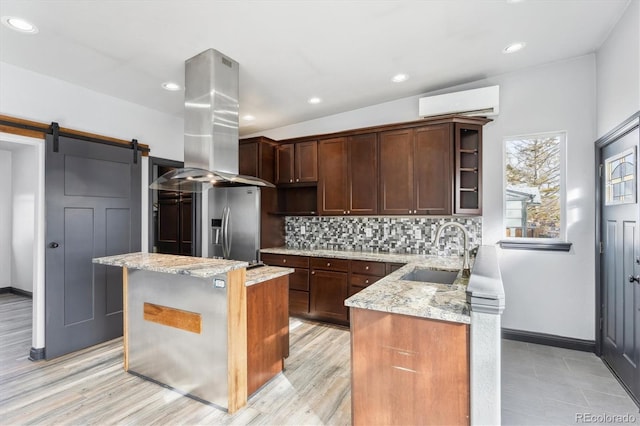 kitchen with tasteful backsplash, a wall mounted air conditioner, a barn door, island exhaust hood, and a sink