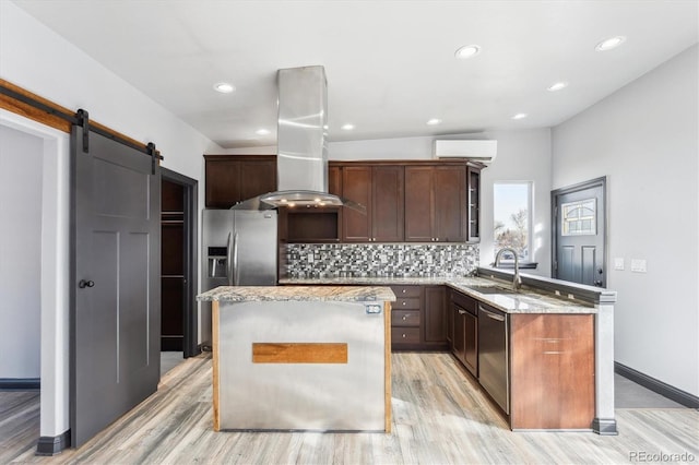 kitchen with a wall mounted AC, a peninsula, a sink, appliances with stainless steel finishes, and island range hood