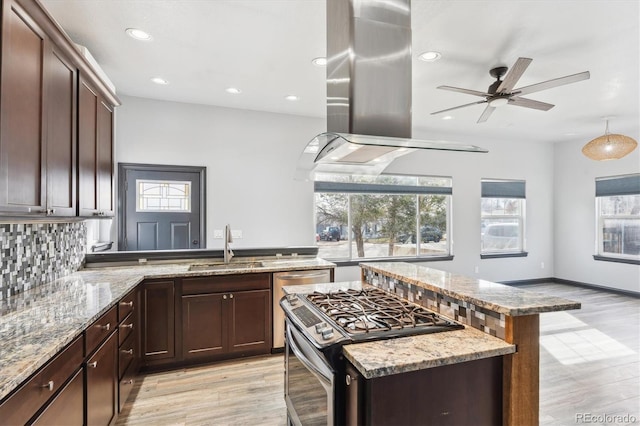 kitchen with a sink, island range hood, decorative backsplash, light stone countertops, and stainless steel gas range