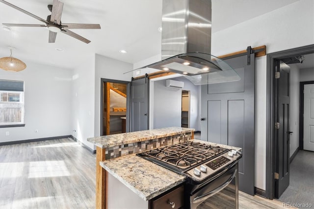 kitchen with island exhaust hood, a barn door, stainless steel gas range, and a wall unit AC