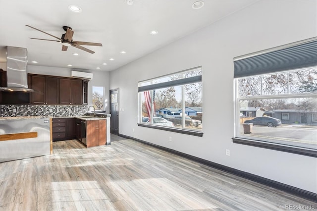 kitchen featuring light wood-type flooring, backsplash, a wall unit AC, island range hood, and light countertops