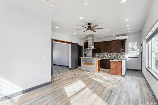 kitchen featuring a kitchen island, a wall mounted air conditioner, a barn door, range hood, and open shelves