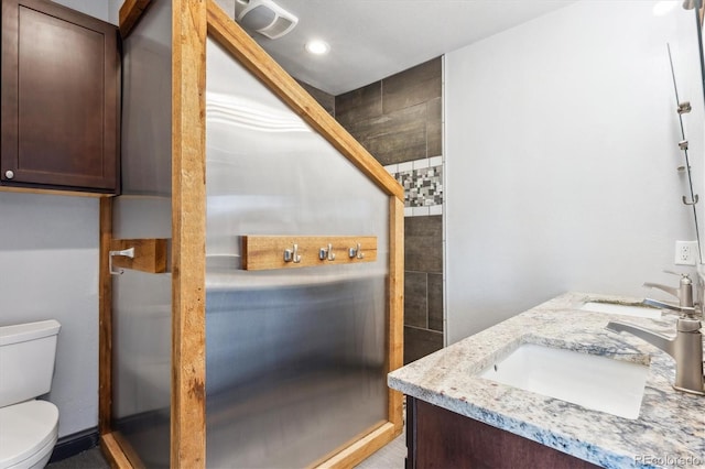 full bath featuring double vanity, a stall shower, toilet, and a sink