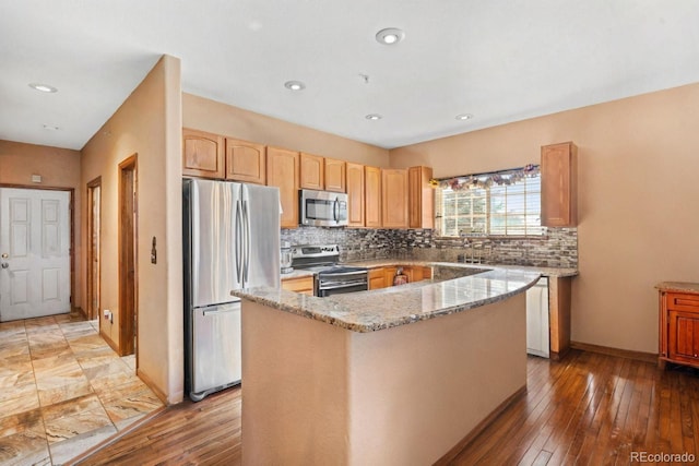 kitchen with light stone countertops, a center island, stainless steel appliances, tasteful backsplash, and light hardwood / wood-style floors