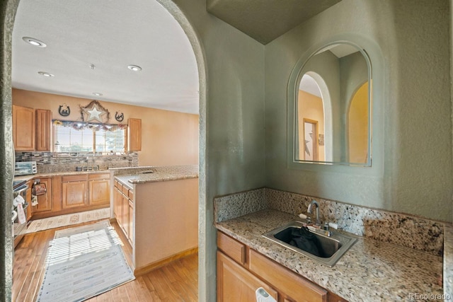 kitchen featuring light wood-style floors, a sink, decorative backsplash, and light stone countertops