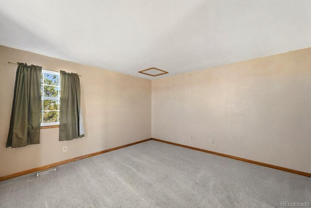 carpeted empty room featuring attic access, visible vents, and baseboards