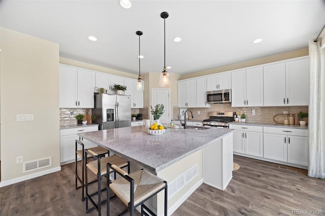 8261 Garden City Ave, Littleton, CO 80125 - kitchen featuring appliances with stainless steel finishes, a sink, decorative backsplash, an island with sink, and white cabinetry
