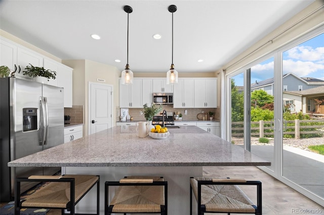 8261 Garden City Ave, Littleton, CO 80125 - kitchen with appliances with stainless steel finishes, decorative backsplash, white cabinets, a kitchen island with sink, and a sink